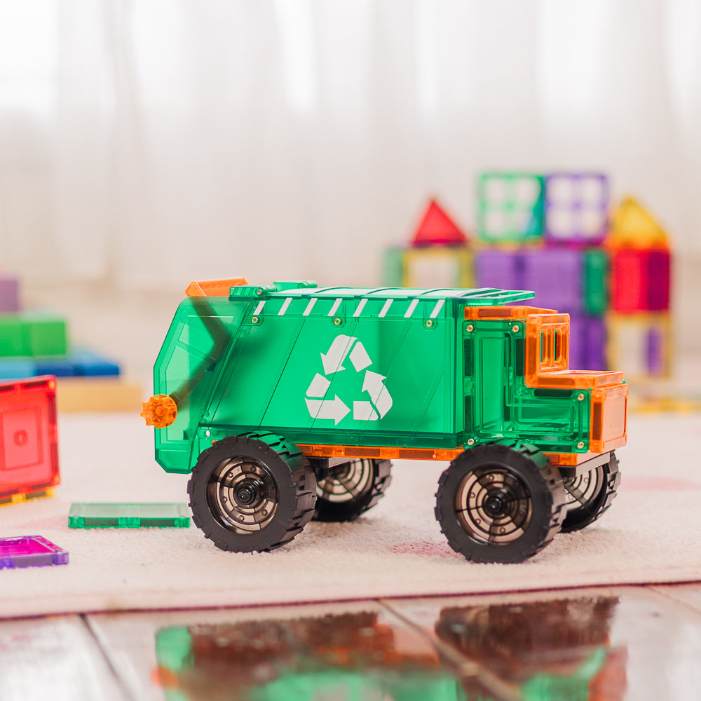 Toy garbage truck with recycling symbol on a reflective surface, colorful blocks in the background