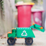Toy magnetic tile  garbage truck with recycling symbol in front of real trash bins.