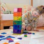 Child playing with colourful magnetic tiles near a bed