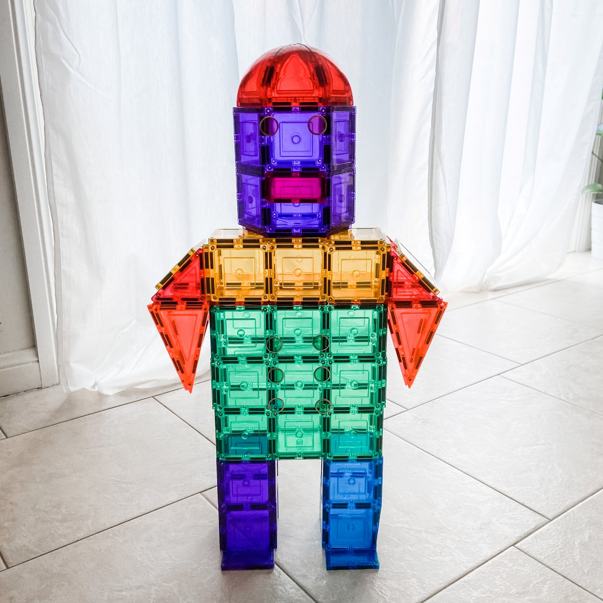 Large rainbow robot made from learn & grow toys dome pack sitting in room with tiles on floor and light streaming in through curtains