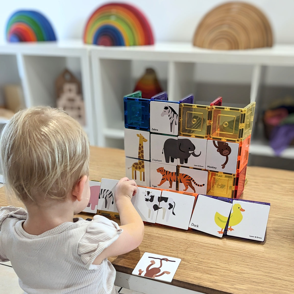 Child playing with the puzzle pack trying to work out the matching animal in a playroom with wooden rainbows in background