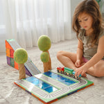 Girl sitting on floor playing with wooden trains on magnetic tiles with train toppers and papoose wooden trees surrounding play set up 